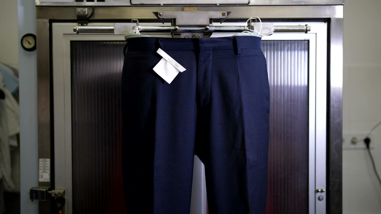 Un pantalone blu appeso alla gruccia con il cartellino di carta attaccato, davanti alla macchina del vapore
