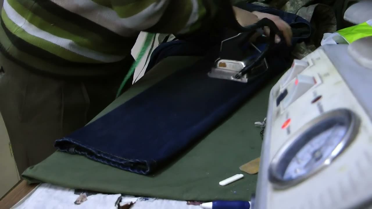 Un ferro da stiro professionale collegato alla caldaia, su un paio di pantaloni stesi sul tavolo da stiro